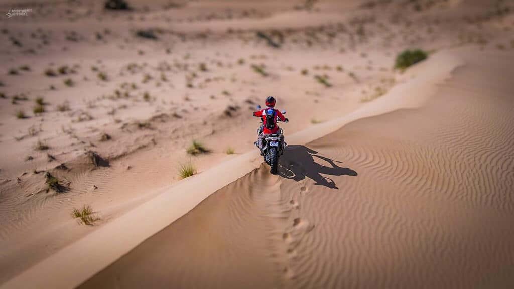 Motorcycle and rider sitting on top of sand dune in desert